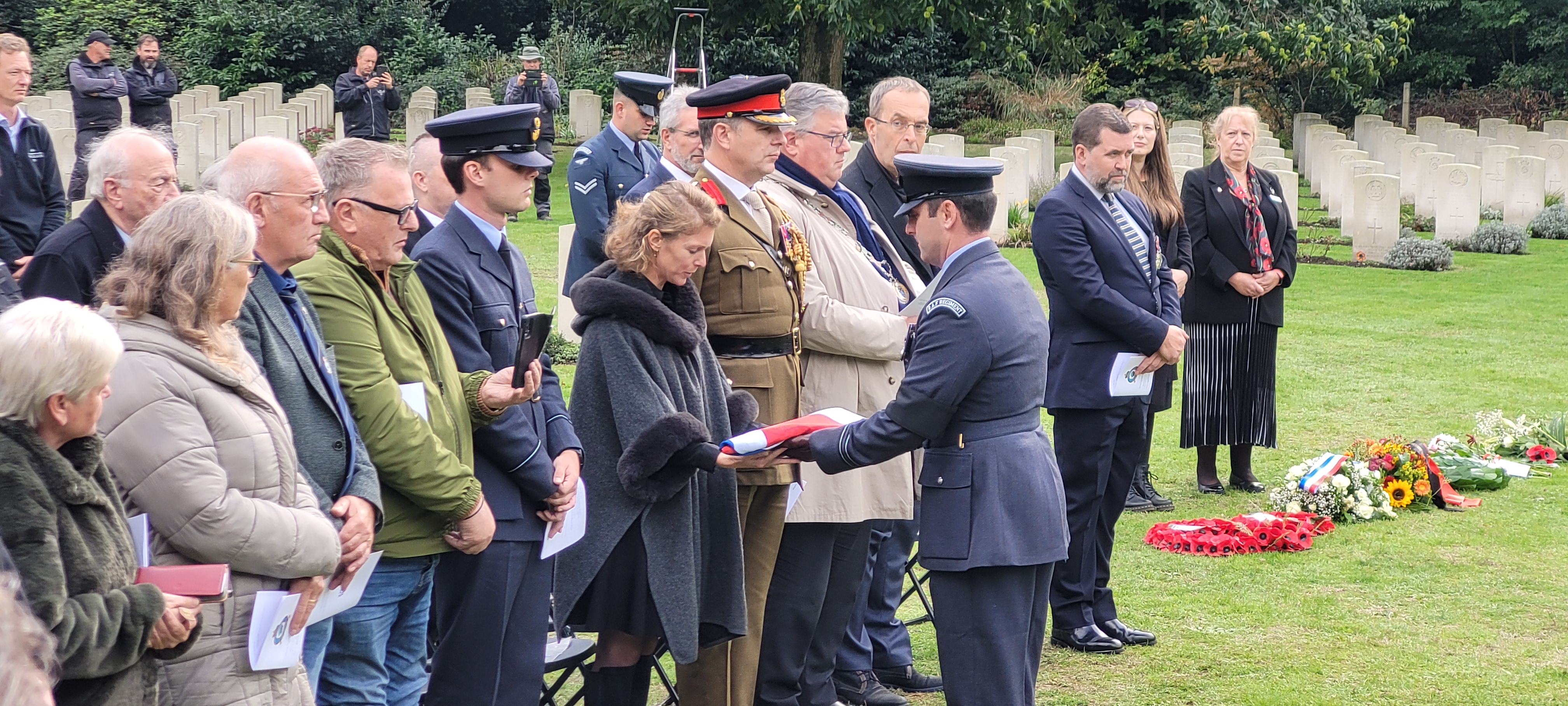 Image of RAF aviators and civilians standing in the cemetery with flower wreaths..